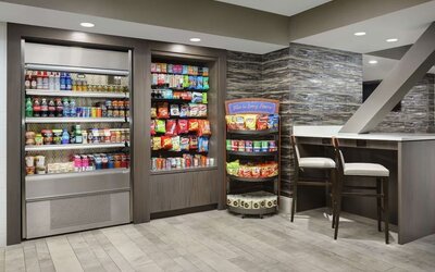 Hotel market offering refrigerated beverages, packaged snacks, pantry items, and casual seating area.