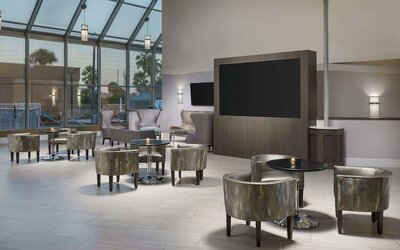 Elegant lobby lounge with armchairs, cocktail tables, soaring glass ceiling, and large display screen.