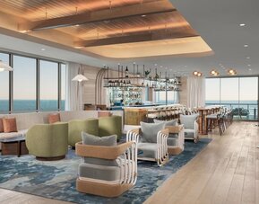 Spacious lounge and bar area with ocean views, plush seating, wood flooring, and contemporary coastal décor.