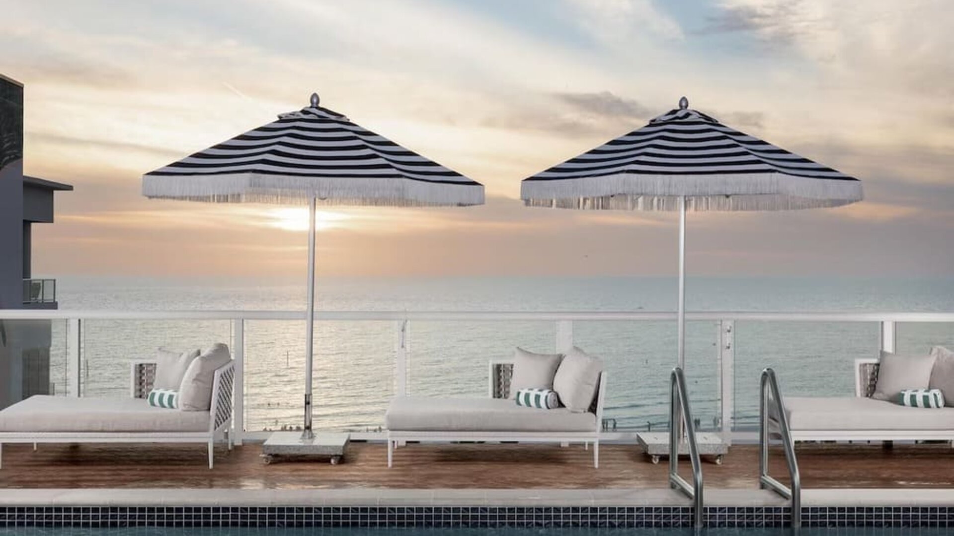 Resort-style pool with shallow tanning ledge, in-water loungers, striped umbrellas, and private cabana seating.
