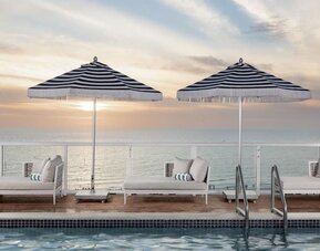 Resort-style pool with shallow tanning ledge, in-water loungers, striped umbrellas, and private cabana seating.