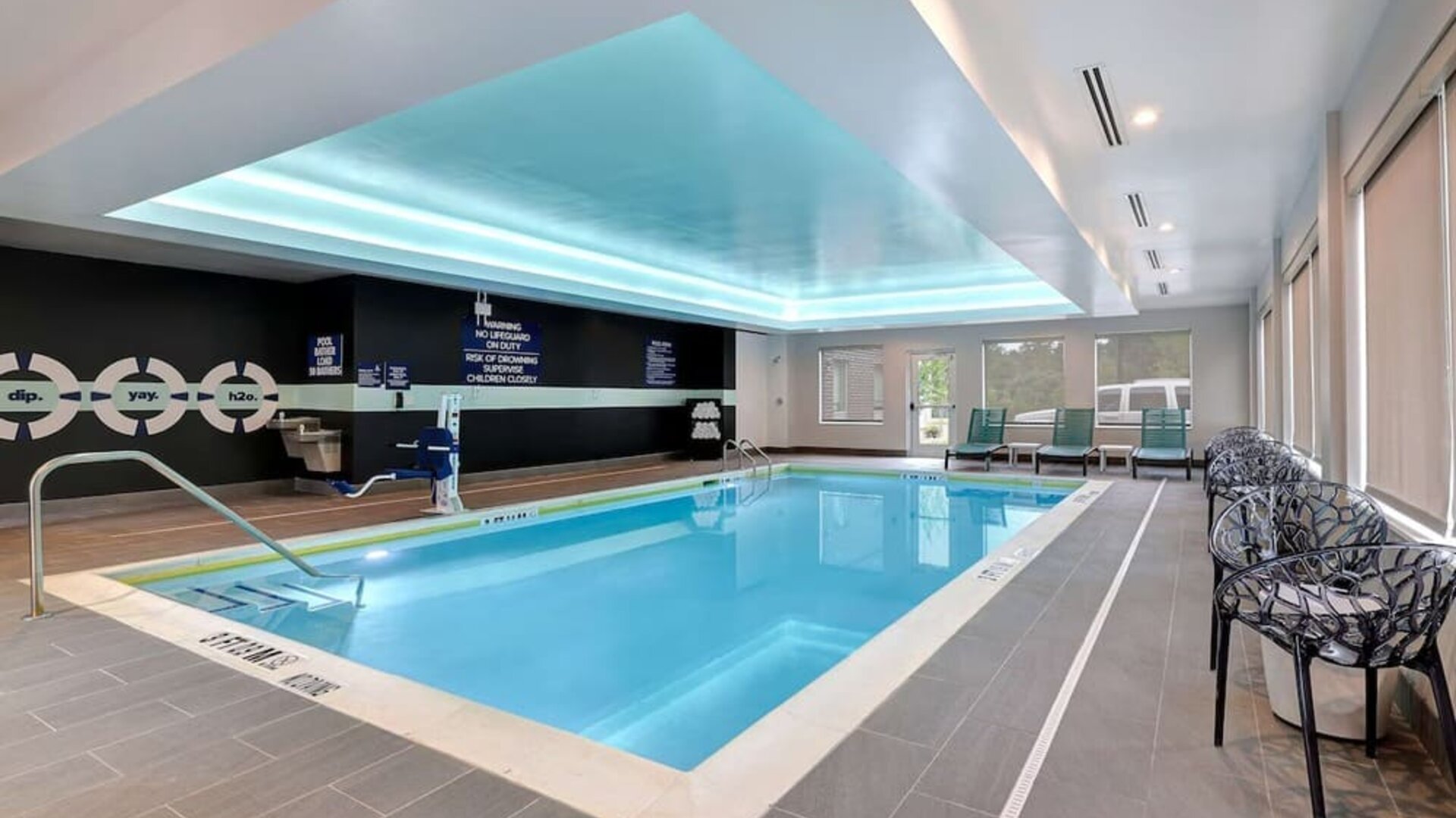 Indoor heated swimming pool with accessible lift, lounge chairs, and natural light at Tru By Hilton Lithia Springs.