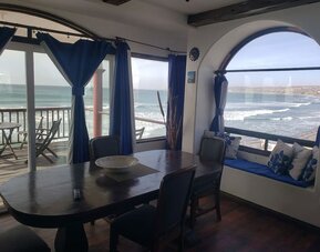 Dining area with panoramic ocean views, large windows, and access to a beachfront balcony at Casa Playa Baja Resort.