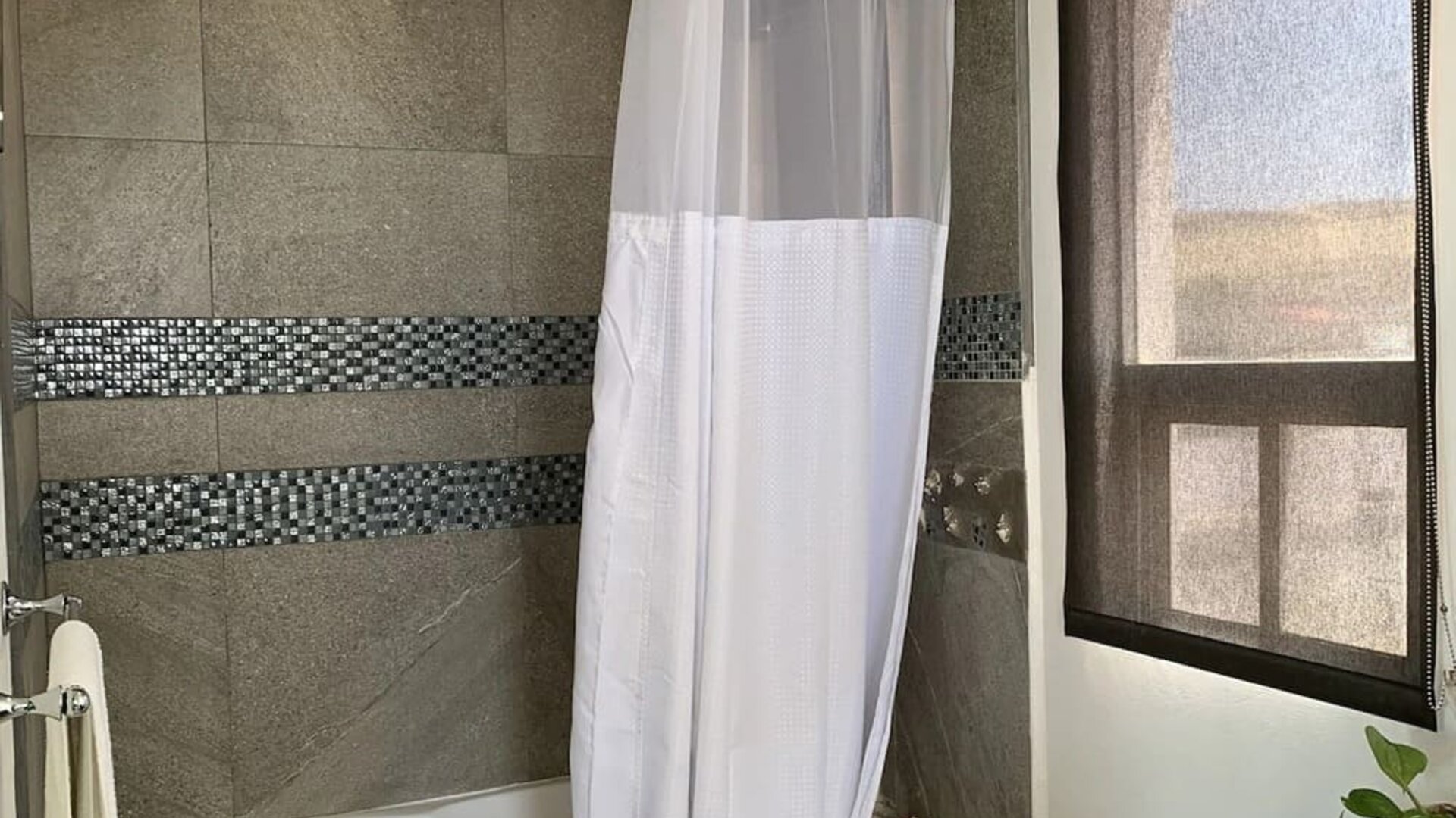 Modern bathroom featuring a bathtub with shower, tiled walls, vanity, and natural light at Casa Playa Baja Resort.
