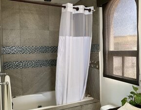 Modern bathroom featuring a bathtub with shower, tiled walls, vanity, and natural light at Casa Playa Baja Resort.