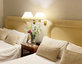 Double guest room with two beds, soft neutral décor, bedside tables, and thoughtful amenities suitable for group or family stays at Hotel Lafayette.