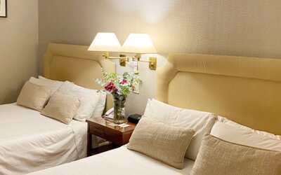 Double guest room with two beds, soft neutral décor, bedside tables, and thoughtful amenities suitable for group or family stays at Hotel Lafayette.