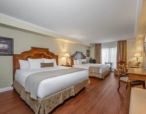 Spacious guest room with two queen beds, work desk and comfortable seating at Hotel Brossard.