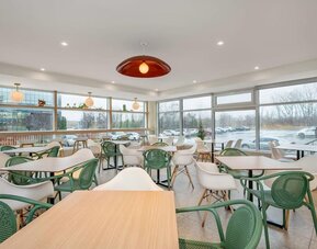 Bright dining area with floor-to-ceiling windows and contemporary seating at Hotel Brossard.