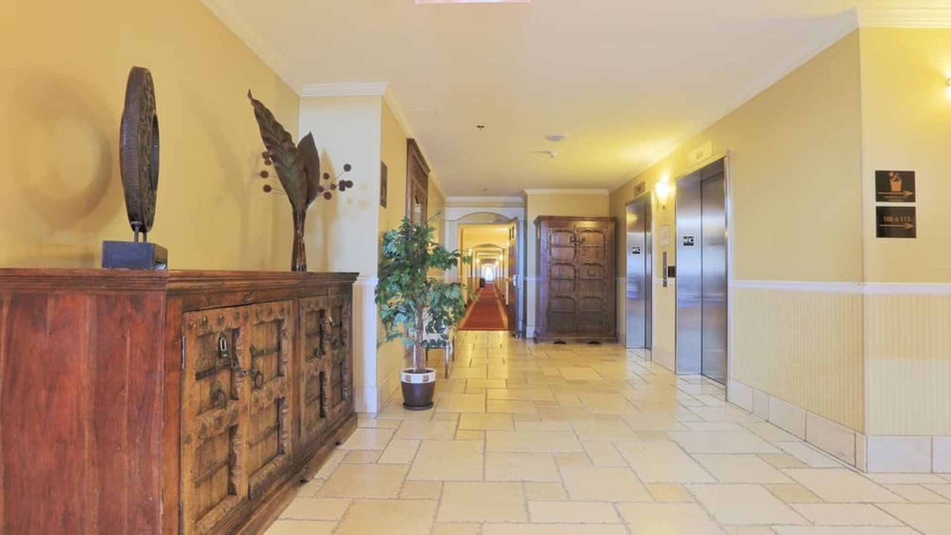 Bright hotel corridor with elevator access and elegant décor at Hotel Brossard.