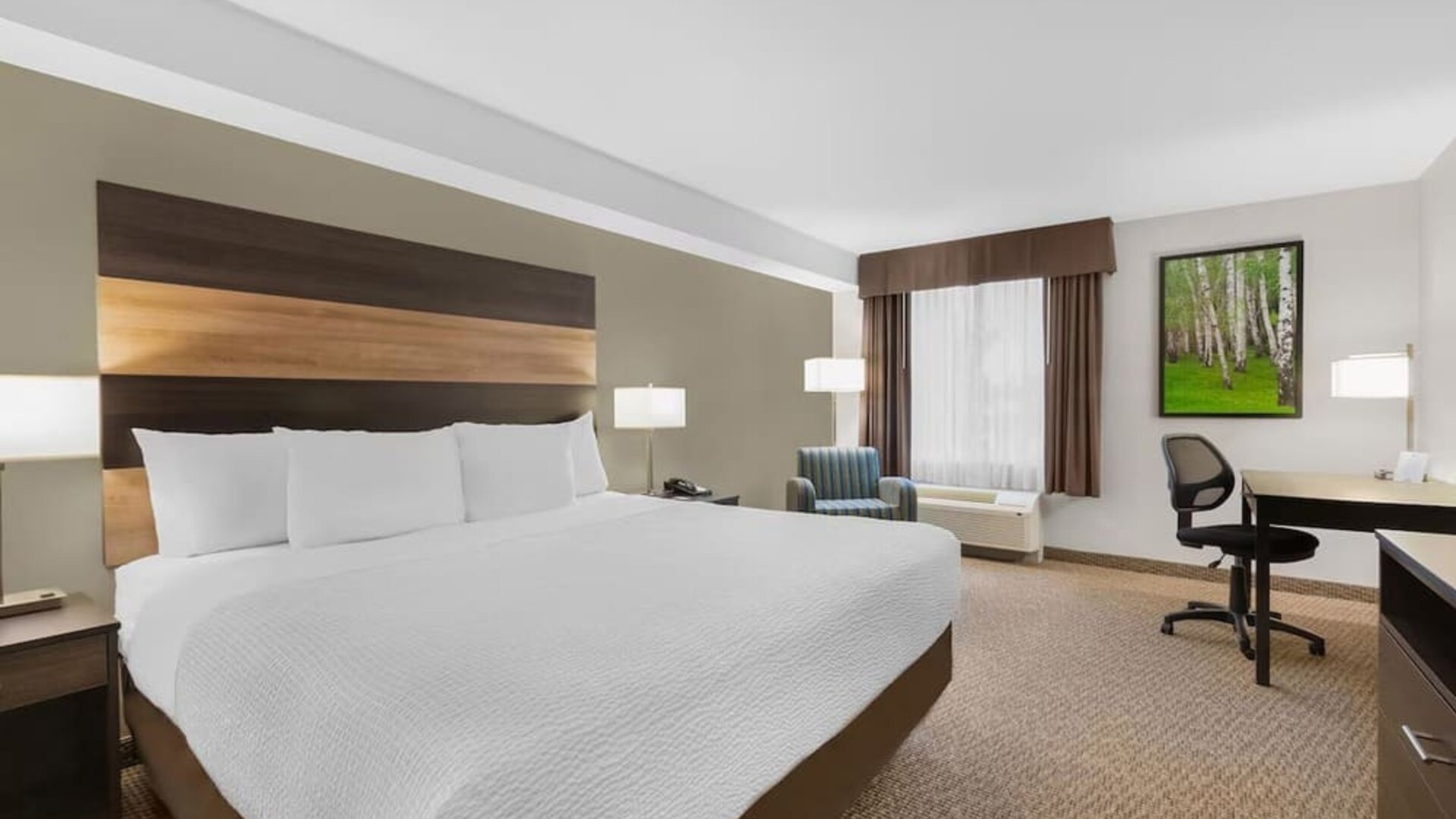 Comfortable king guest room with workspace, armchair and modern amenities at Days Inn & Suites By Wyndham Lindsay.
