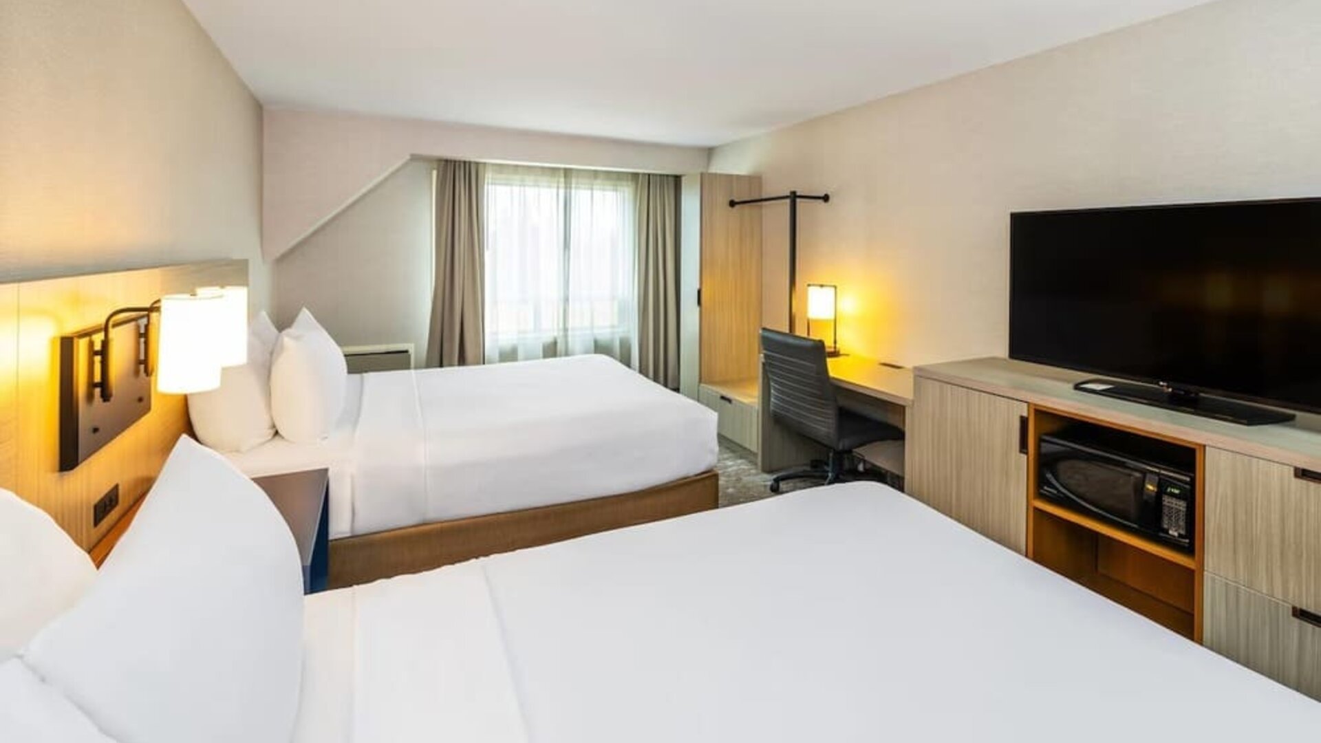 Spacious guest room with two queen beds, flat-screen TV, work desk, microwave, and mini fridge at Comfort Inn Amherst.