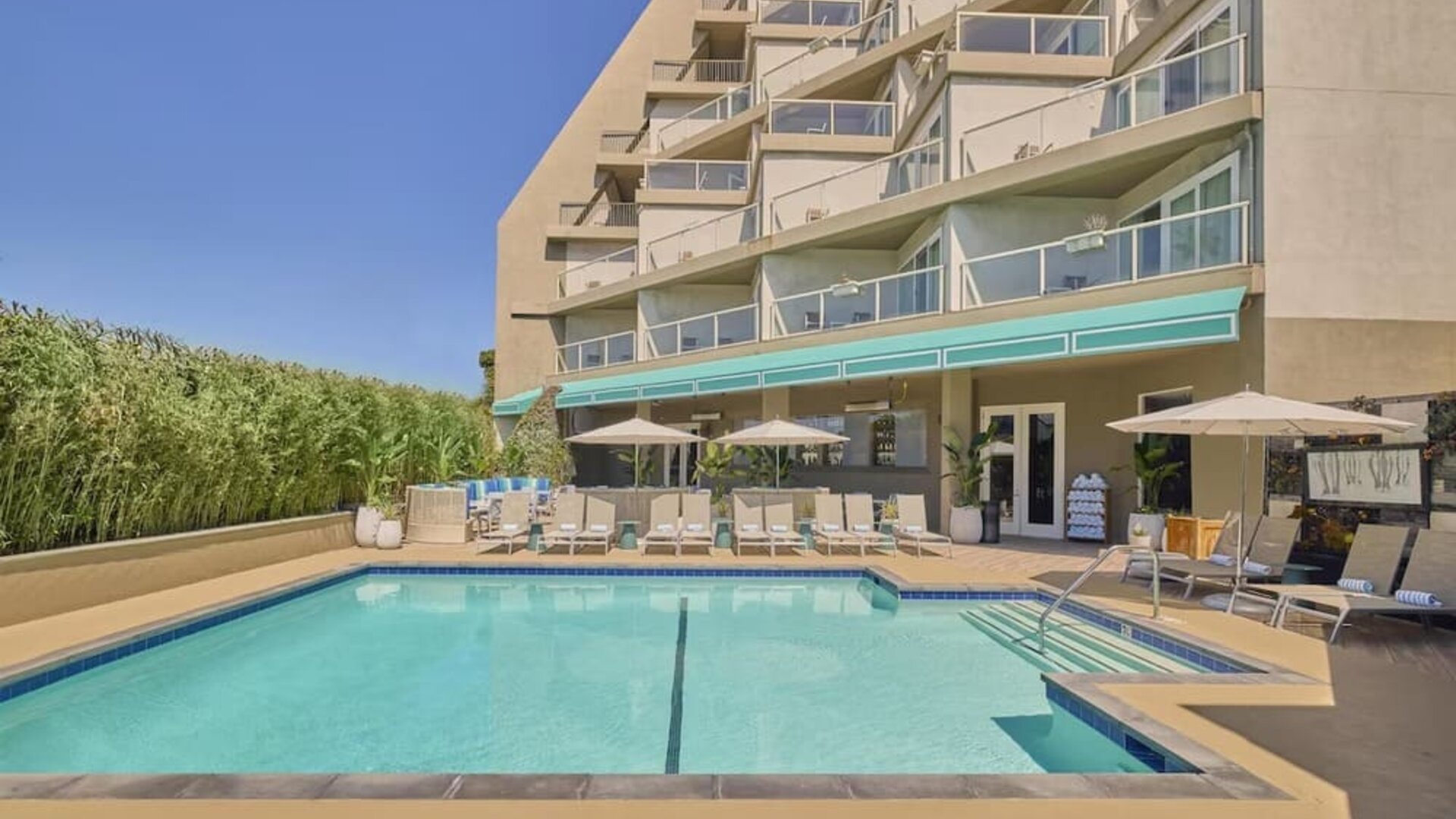 Outdoor swimming pool surrounded by lounge chairs, shaded seating, and relaxing spaces to enjoy the California sunshine at Hyatt Centric Delfina Santa Monica.