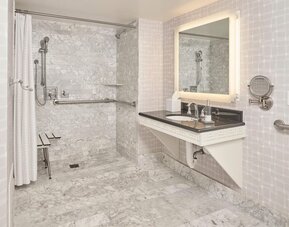 Accessible marble bathroom with roll-in shower, grab bars, illuminated vanity, and spacious design at Hyatt Centric Delfina Santa Monica.