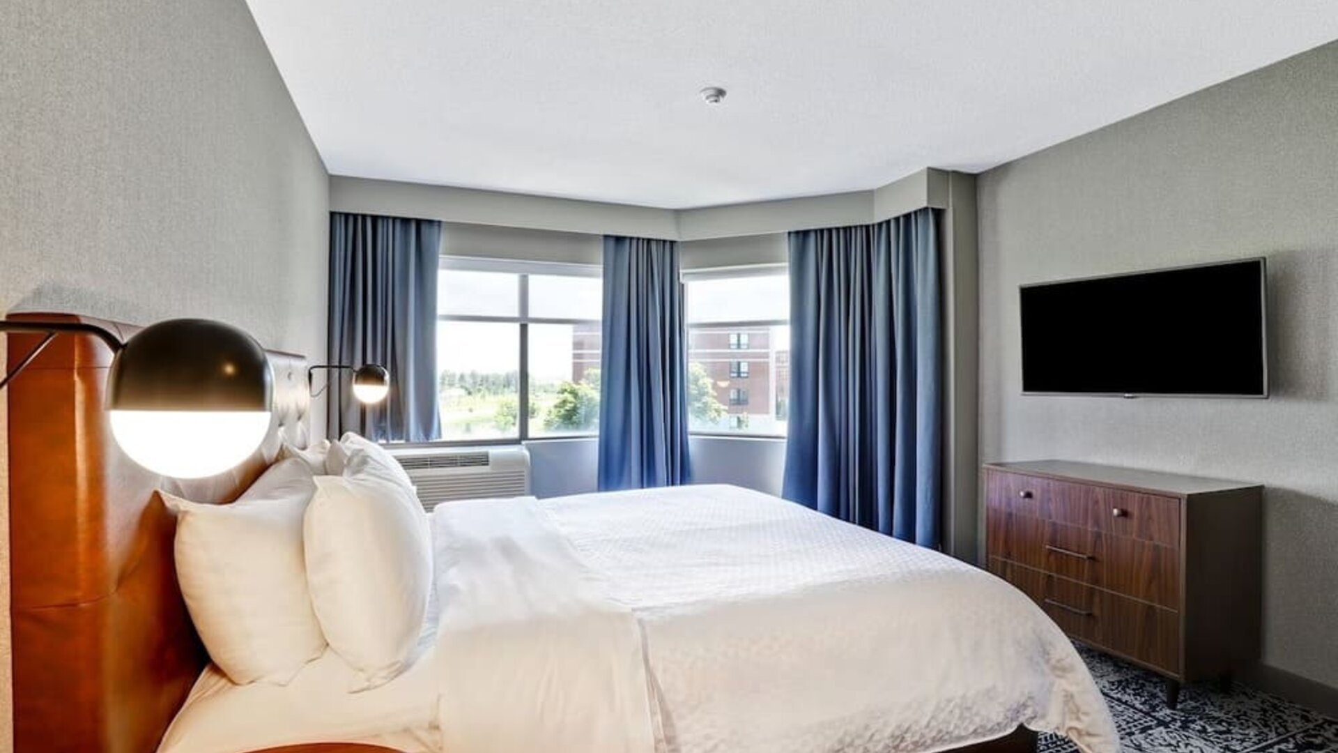 Bright king guest room with large windows, modern furnishings, and city views at Four Points by Sheraton St. Catharines Niagara Suites.