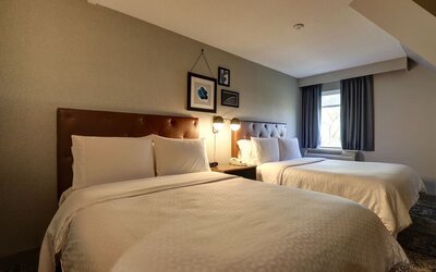 Spacious guest room with two queen beds, comfortable furnishings, and modern décor at Four Points by Sheraton St. Catharines Niagara Suites.