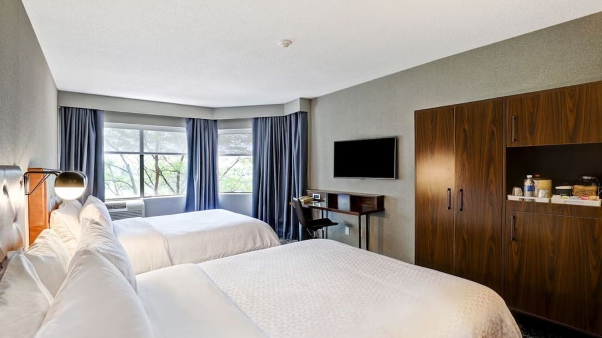 Spacious guest room featuring two plush beds, a large flat-screen TV, and modern furnishings at Four Points by Sheraton St. Catharines Niagara Suites.