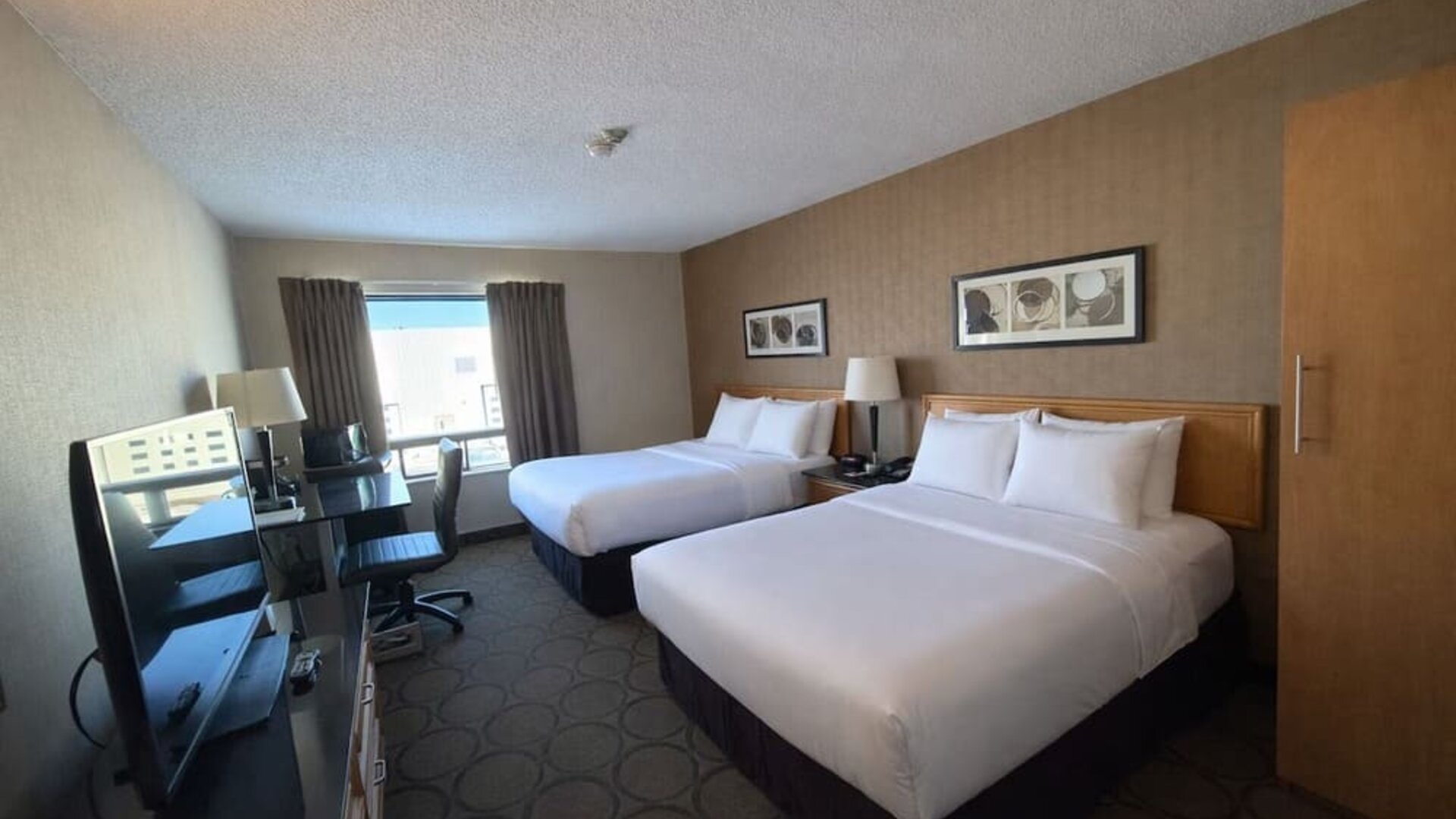 Double queen guest room offering two plush beds, workspace, flat-screen TV, and plenty of natural light at Comfort Inn Baie-Comeau.