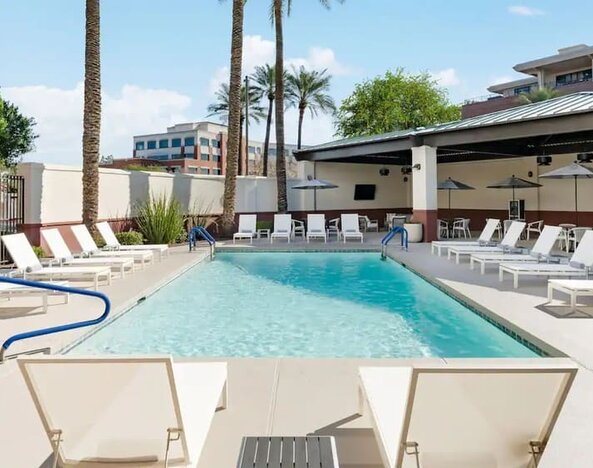 Outdoor swimming pool surrounded by lounge chairs, shaded seating, and sunny relaxation spaces at Hyatt Place Scottsdale/Old Town.