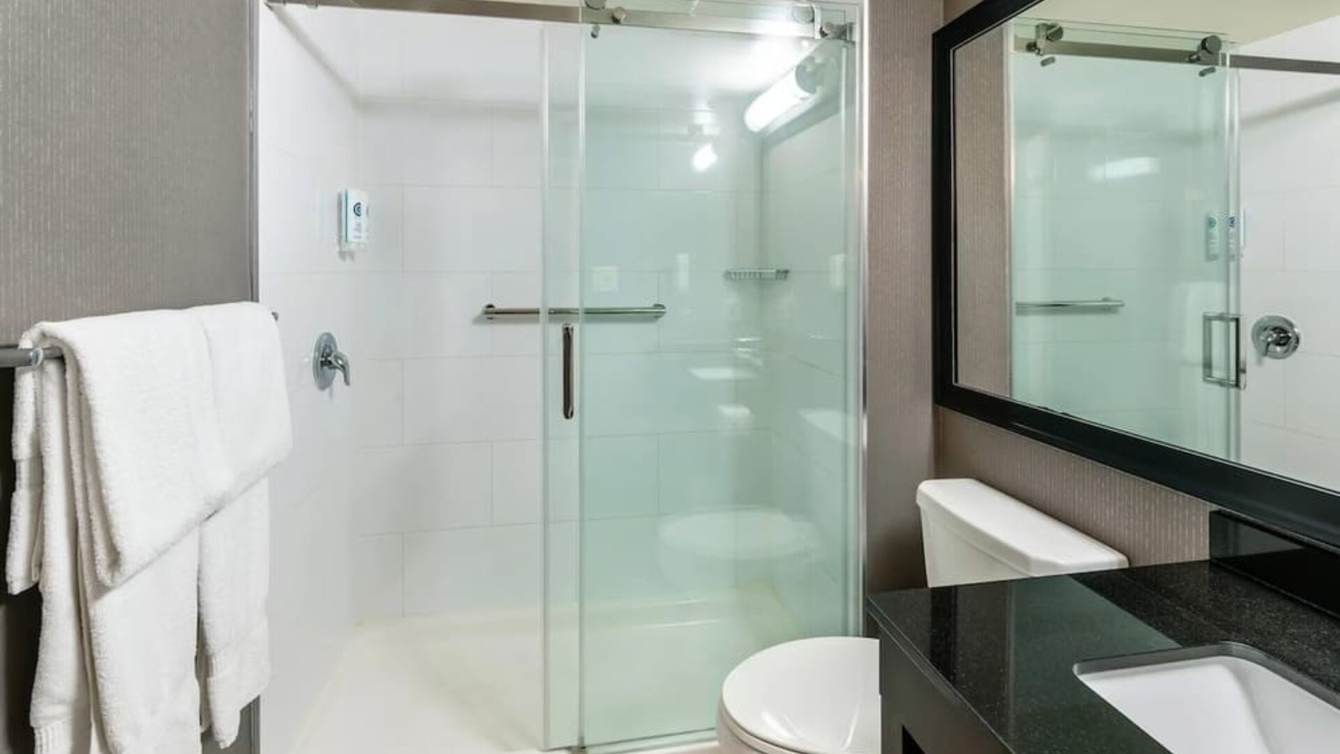 Modern guest bathroom featuring a glass walk-in shower, granite vanity, fresh towels, and contemporary finishes at Comfort Inn Sudbury Regent Street.