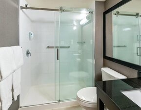 Modern guest bathroom featuring a glass walk-in shower, granite vanity, fresh towels, and contemporary finishes at Comfort Inn Sudbury Regent Street.