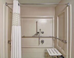 Accessible roll-in shower with grab bars and a shower seat at Hampton Inn & Suites By Hilton Guelph.