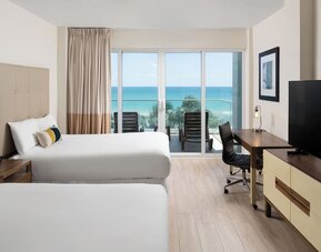 Oceanfront guest room with two beds, workspace, and private balcony at Sherry Frontenac Oceanfront Hotel.