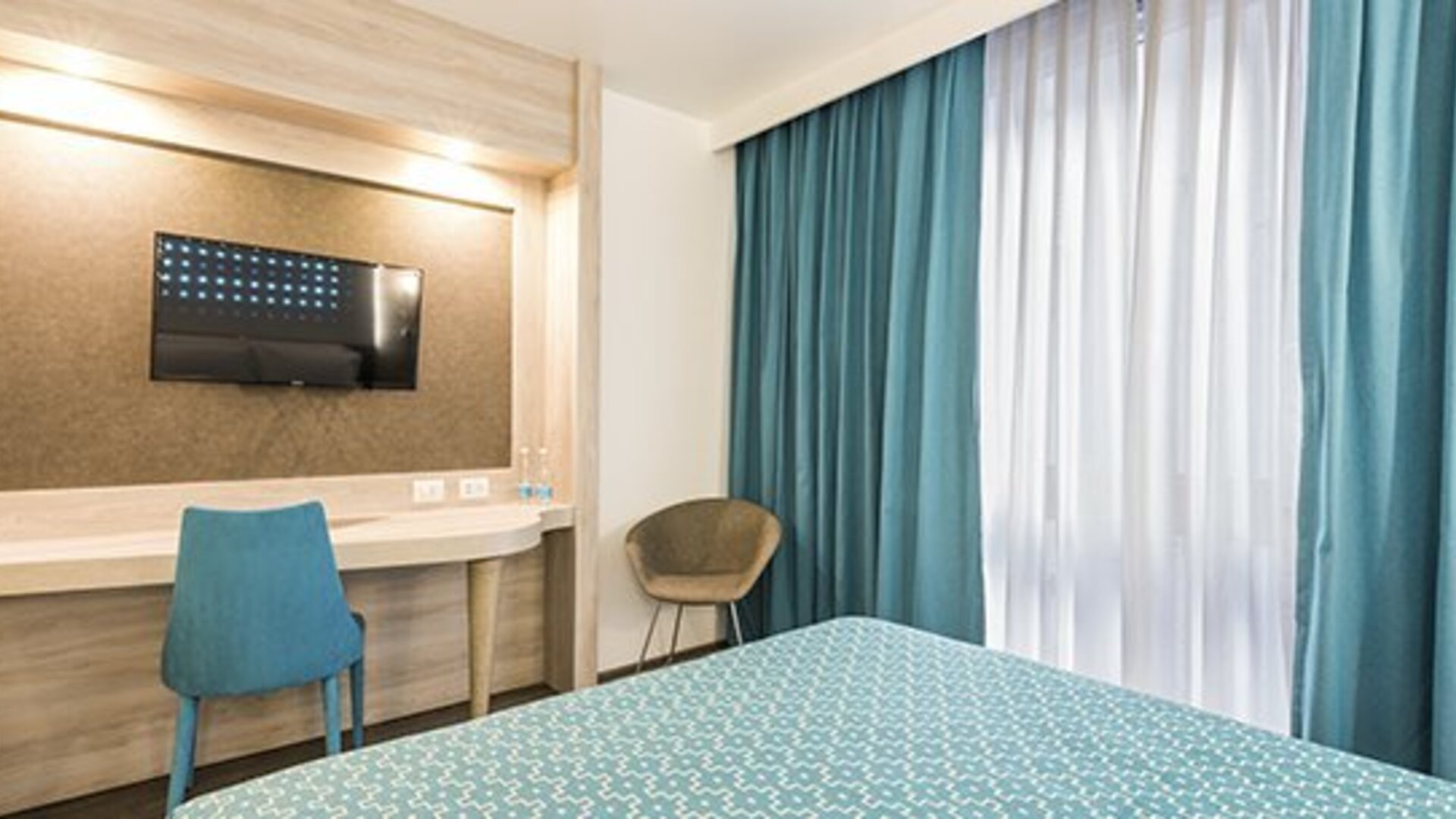 Guest room workspace with wall-mounted TV, desk, chair and floor-to-ceiling curtains at Hotel Casa Blanca.