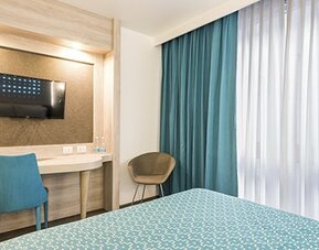 Guest room workspace with wall-mounted TV, desk, chair and floor-to-ceiling curtains at Hotel Casa Blanca.