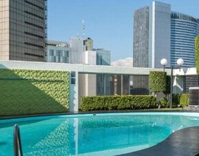 Outdoor swimming pool surrounded by landscaped greenery with high-rise city buildings beyond at Hotel Casa Blanca.