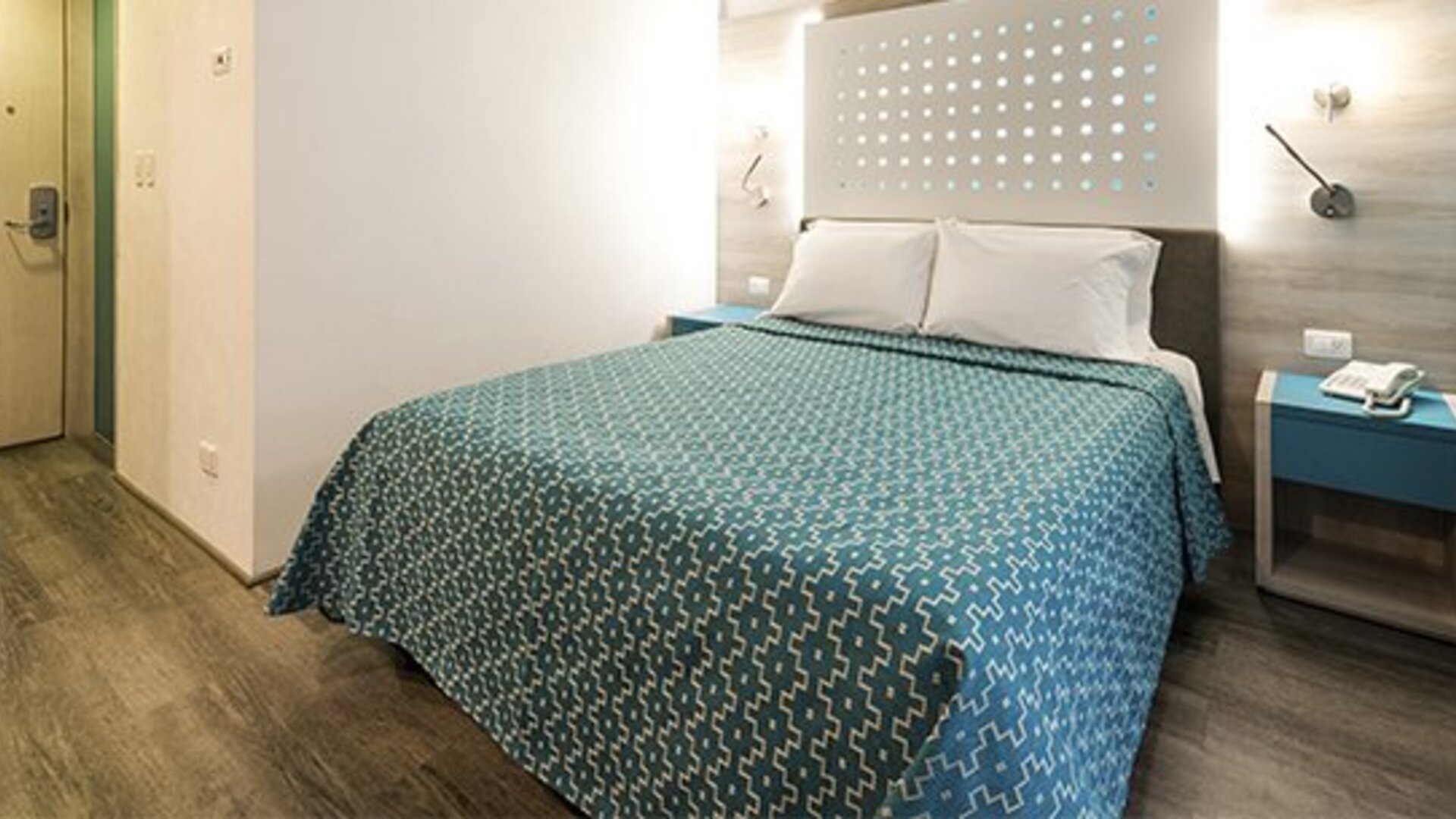Guest room with a queen bed, illuminated headboard, bedside table and wood-look flooring at Hotel Casa Blanca.