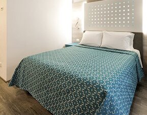 Guest room with a queen bed, illuminated headboard, bedside table and wood-look flooring at Hotel Casa Blanca.