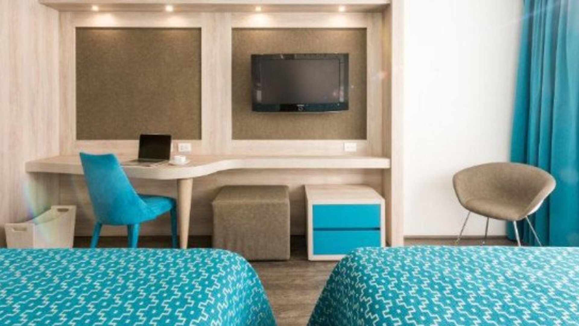 Guest room with two beds, workspace, wall-mounted TV and blue accent furnishings at Hotel Casa Blanca.