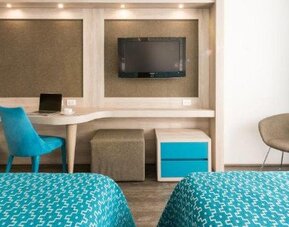 Guest room with two beds, workspace, wall-mounted TV and blue accent furnishings at Hotel Casa Blanca.