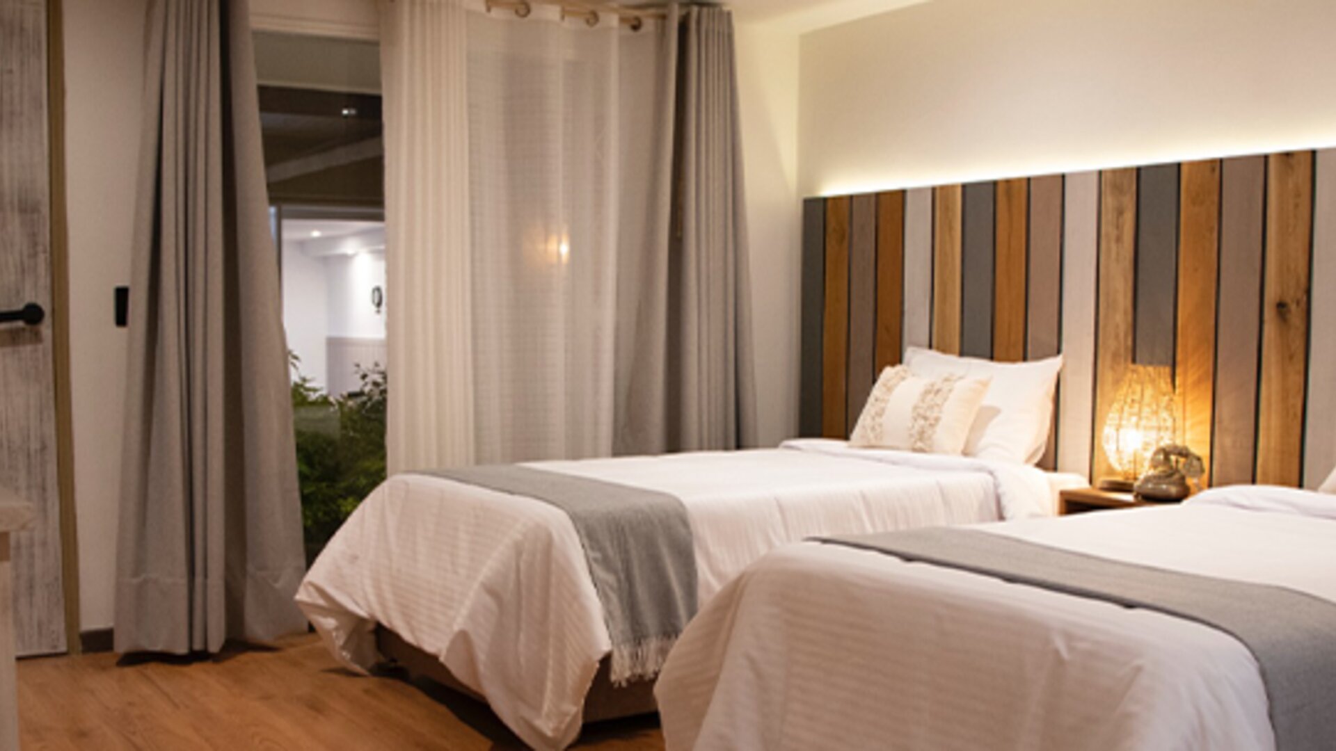 Spacious guest room with two beds, wood flooring and large curtains overlooking the courtyard at Marbore Hotel & Spa.