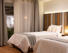 Spacious guest room with two beds, wood flooring and large curtains overlooking the courtyard at Marbore Hotel & Spa.