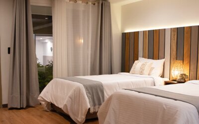 Spacious guest room with two beds, wood flooring and large curtains overlooking the courtyard at Marbore Hotel & Spa.