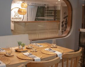 Contemporary dining area with wooden tables, woven placemats and views of the reception area at Marbore Hotel & Spa.