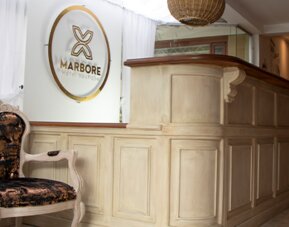 Elegant reception desk with carved wood finishes, decorative seating and Marbore Hotel Boutique signage at Marbore Hotel & Spa.
