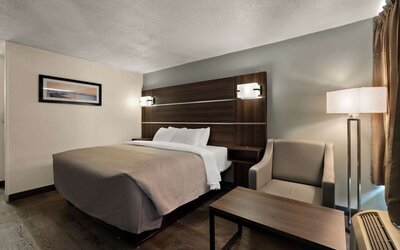 Guest room with one king bed, armchair, coffee table and floor lamp beside the window at Quality Inn Yemassee - Point South I-95.