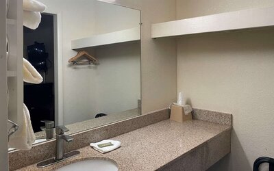 Bathroom vanity with granite countertop, large mirror, open shelving and hanging space at Econo Lodge Yemassee.