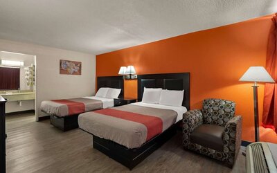Guest room with two double beds, accent wall, armchair and open vanity area at Econo Lodge Yemassee.