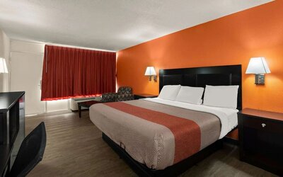 King guest room with orange accent wall, blackout curtains and workspace at Econo Lodge Yemassee.