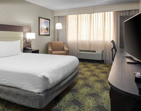King guest room with plush bed, HDTV, armchair, workspace, and large windows providing natural daylight.