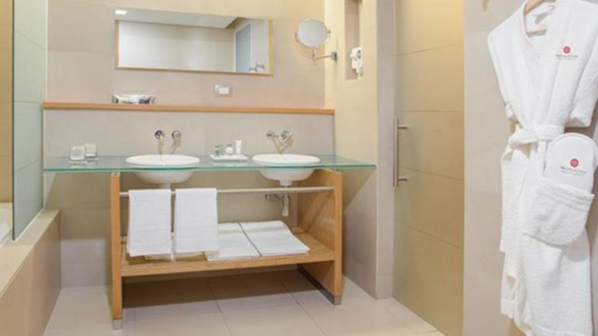 Modern bathroom with double vanity, bathtub, glass countertop and premium bath amenities at NH Collection Mexico City Airport T2.