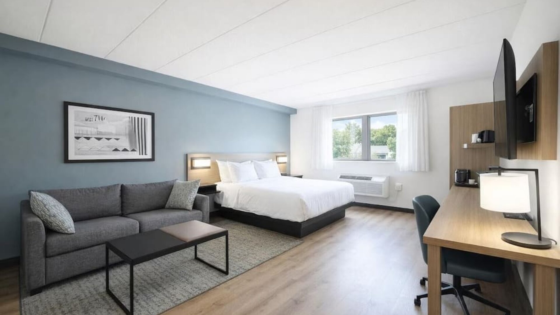 Bright guest room with a king bed, sofa, work desk and large windows providing plenty of natural light at Hyatt Select Philadelphia Airport.