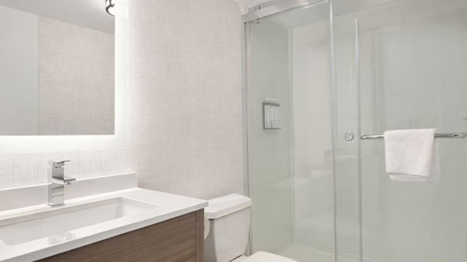 Modern guest bathroom featuring a walk-in glass shower, illuminated vanity mirror, spacious sink and complimentary toiletries at Hyatt Select Philadelphia Airport.