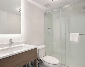 Modern guest bathroom featuring a walk-in glass shower, illuminated vanity mirror, spacious sink and complimentary toiletries at Hyatt Select Philadelphia Airport.