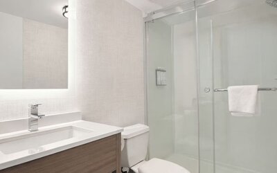 Modern guest bathroom featuring a walk-in glass shower, illuminated vanity mirror, spacious sink and complimentary toiletries at Hyatt Select Philadelphia Airport.