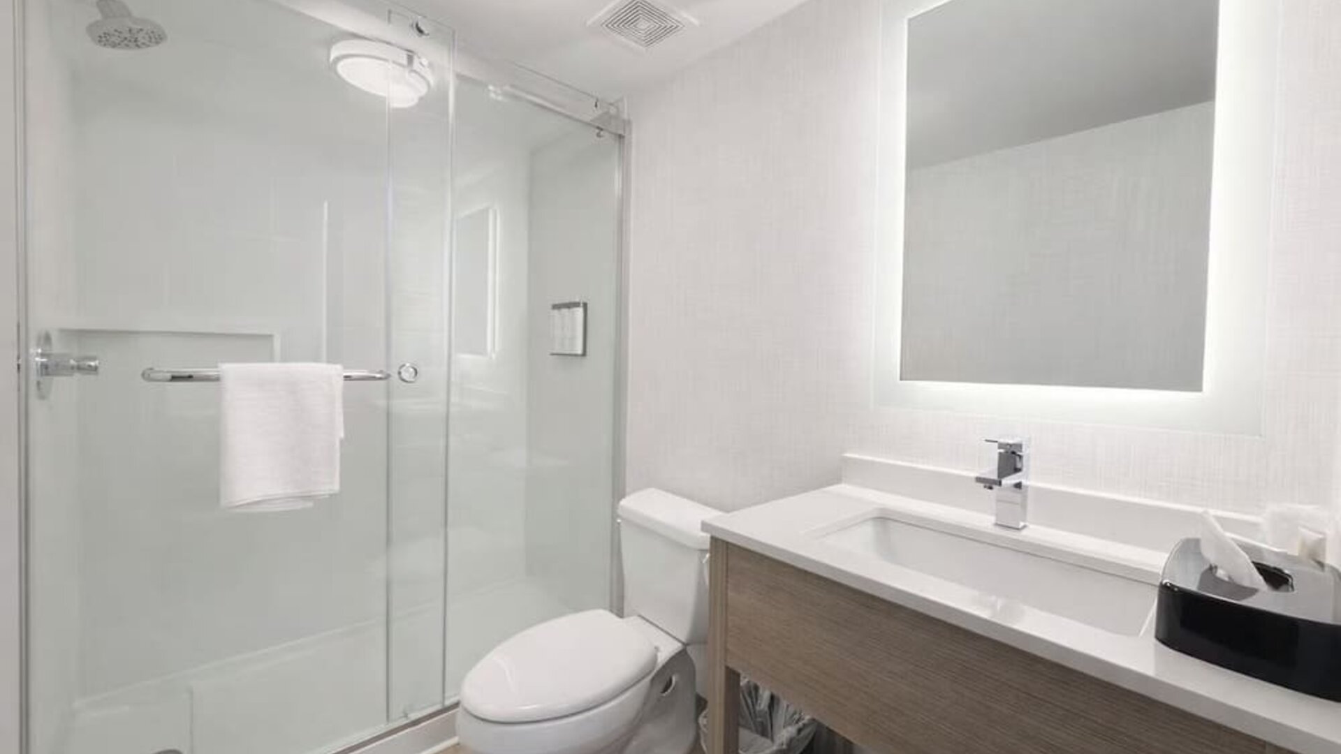 Contemporary guest bathroom featuring a walk-in glass shower, modern vanity, illuminated mirror and fresh towels at Hyatt Select Philadelphia Airport.